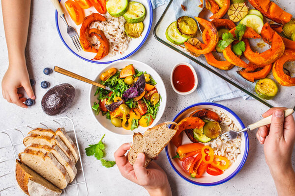 Flat lay of family hands eating healthy food. Vegan lunch table top view. Baked vegetables, fresh salad, berries, bread on a white background.