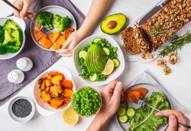 Sağlıklı vegan gıda yemek, üstten görünüm. Vejetaryen yemek masası, insanlar sağlıklı yemek yemek. Salata, tatlı patates, vegan kek, beyaz bir arka plan üzerinde sebze.