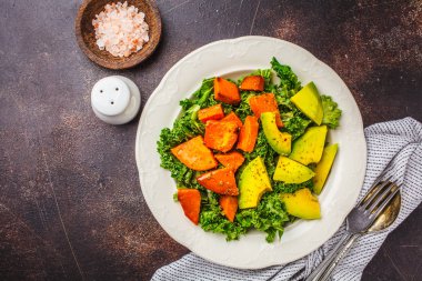 Avokado ve pişmiş tatlı patates sağlıklı yeşil lahana salatası. Göre diyet kavramı bitki, gıda detoks. Üstten görünüm, koyu arka plan.