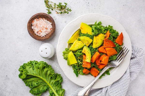 Healthy green kale salad with avocado and baked sweet potatoes. Plant based diet concept, detox food. Top view, white background.