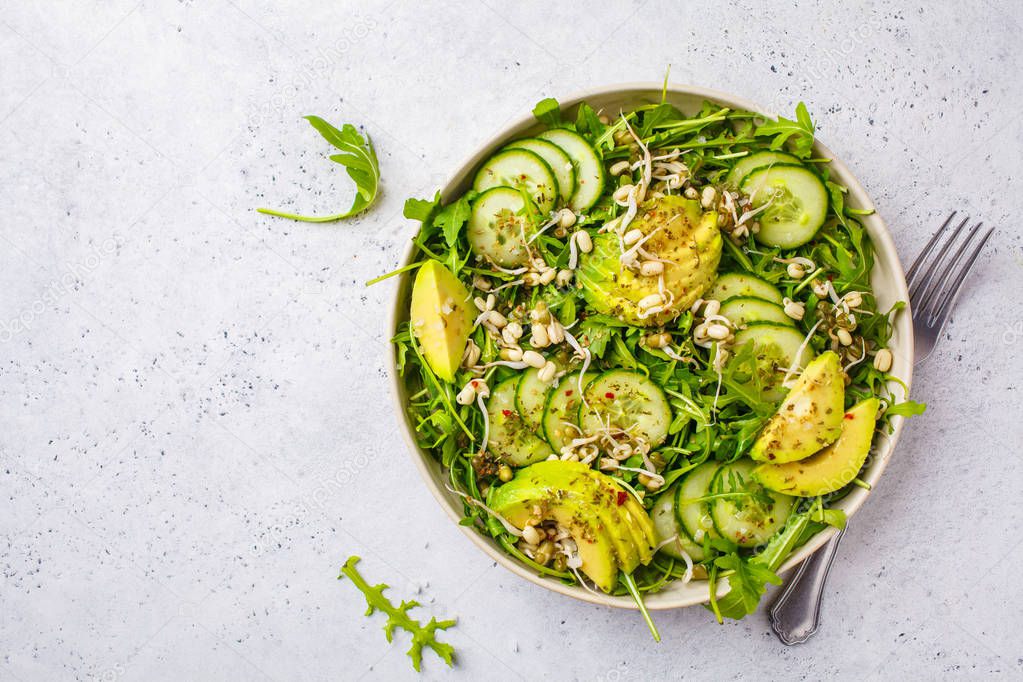 Healthy green salad with avocado, cucumber and arugula in white dish. Plant based diet concept.