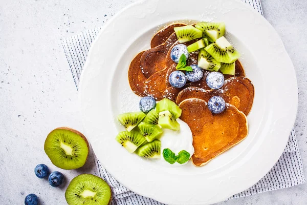 Pancakes in the shape of a heart with berries, fruits and curd cream in a white plate, top view. Valentine's day concept.