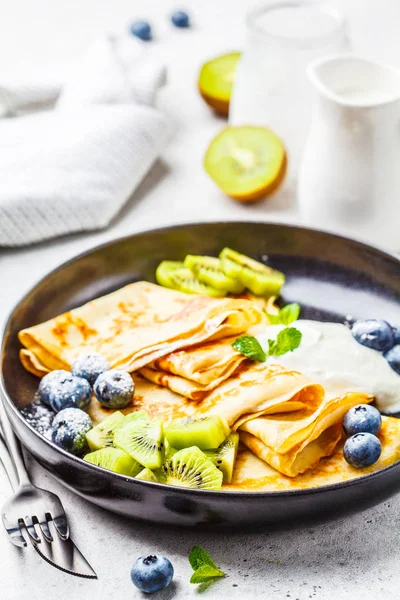 Thin crepes with curd cream, kiwi and blueberries in a black plate. Russian cuisine concept.