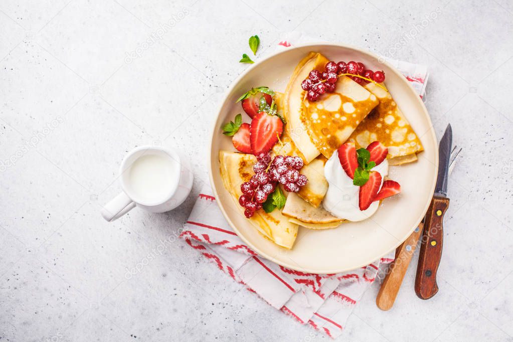 Homemade thin pancakes served with curd cream, currants, strawberries and powdered sugar in white plate. Healthy beautiful breakfast concept.
