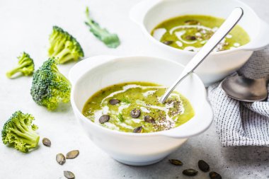 Vegan detoks kremalı brokoli çorbası ile Hindistan cevizi kreması ve kabak tohumu beyaz bir kase. Bitki esaslı gıda kavramı.