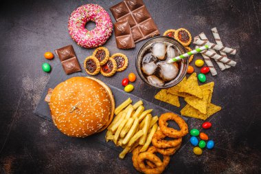 Abur cubur kavramı. Sağlıksız yiyecek arka plan. Fast food ve şeker. Hamburger, şekerleme, cips, çikolata, çörek, karanlık bir arka plan üzerine soda.