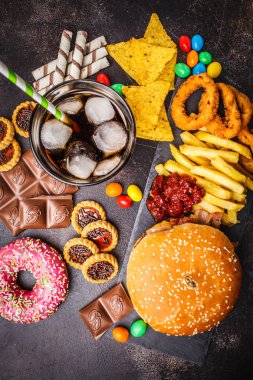 Abur cubur kavramı. Sağlıksız yiyecek arka plan. Fast food ve şeker. Hamburger, şekerleme, cips, çikolata, çörek, karanlık bir arka plan üzerine soda.