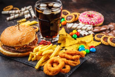 Abur cubur kavramı. Sağlıksız yiyecek arka plan. Fast food ve şeker. Hamburger, şekerleme, cips, çikolata, çörek, karanlık bir arka plan üzerine soda.