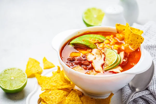 Mexican soup with beans, chicken, corn and nachos in white bowls. Chili con carne - traditional mexican food.