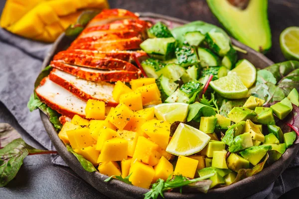 Grilled chicken, mango and avocado salad in a dark dish on dark background.