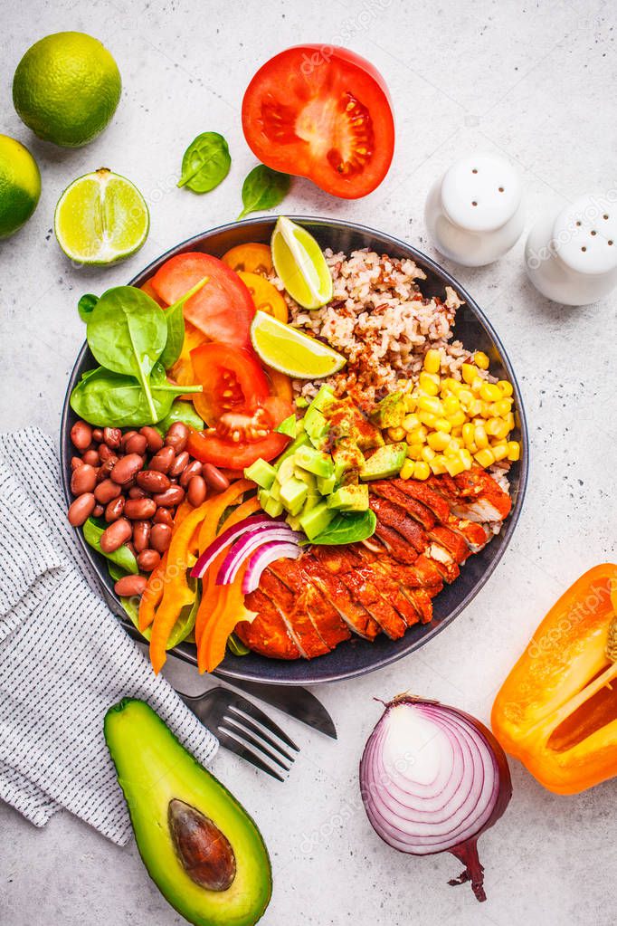 Mexican chicken burrito bowl with rice, beans, tomato, avocado,corn and spinach, white background. Mexican cuisine food concept.