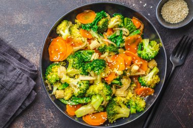 Vegan wok stir fry with broccoli and carrot in black dish, dark backgrond. clipart