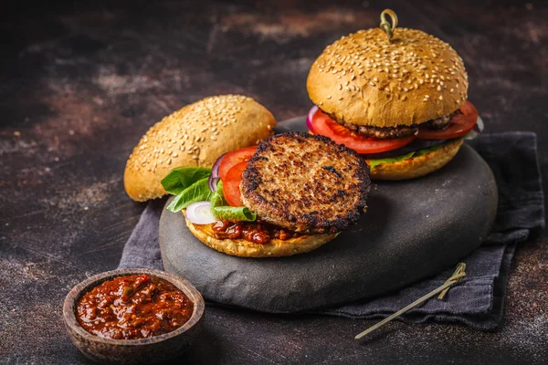 Homemade open burgers with meat and vegetables on a dark background.
