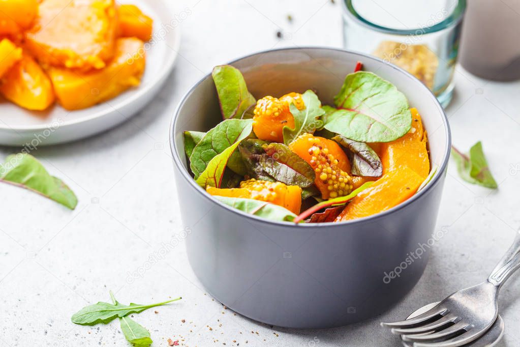 Green salad with pumpkin and mustard in a gray bowl. Healthy vegan food concept.