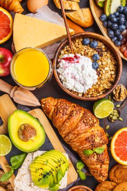 Karanlık bir arka plan üzerinde sağlıklı dengeli kahvaltı. Müsli, süt, meyve suyu, kruvasan, peynir, bisküvi ve meyve, üstten görünüm.