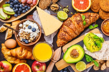 Karanlık bir arka plan üzerinde sağlıklı dengeli kahvaltı. Müsli, süt, meyve suyu, kruvasan, peynir, bisküvi ve meyve, üstten görünüm.