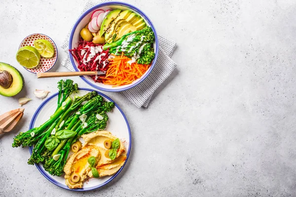 Vegan lunch concept. Rainbow vegetable salad and broccolini with hummus, top view.