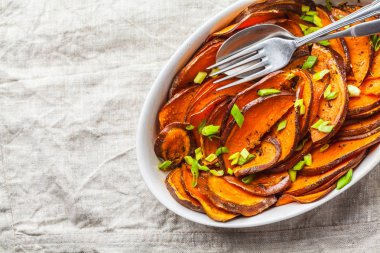 Beyaz tabak içinde yeşil soğan ile dilimlenmiş tatlı patates pişmiş.