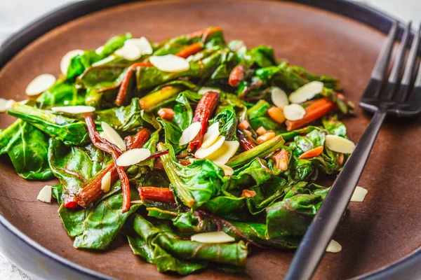 Beet greens salad with nuts in black plate. Healthy vegan food c