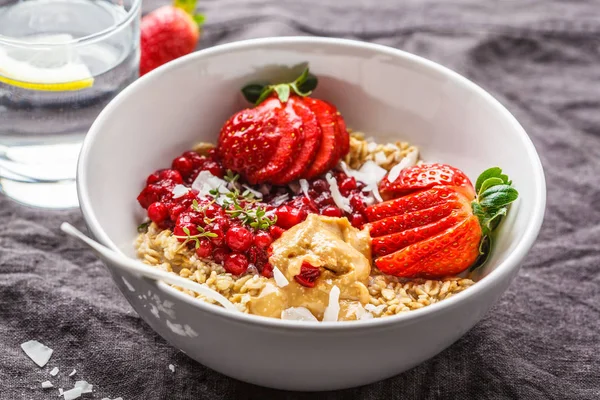 Oatmeal porridge with berries, peanut butter and coconut in whit