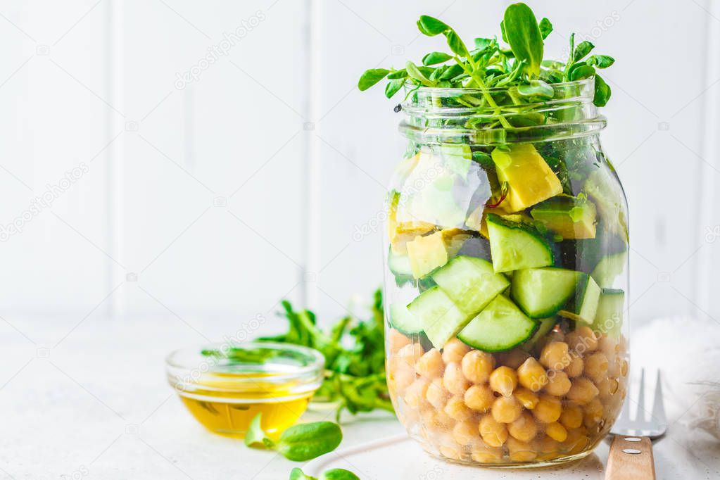 Green salad with chickpeas in a jar, white background, copy spac