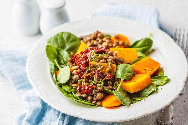 Vegan salad with lentils, pumpkin and dried tomatoes in white pl