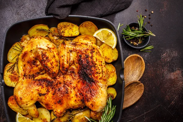 Roasted whole chicken with potatoes in a grill pan, dark backgro