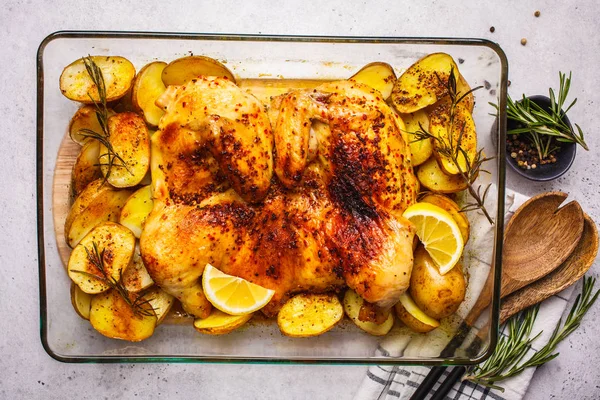 Roasted whole chicken with potatoes in a glass oven dish, top vi