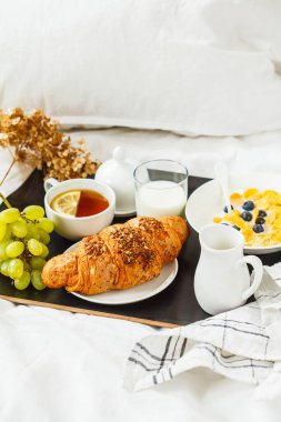 Yatakta kontinental kahvaltı. Kruvasan, mısır gevreği, çay, süt bir