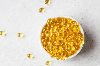 Balık yağı kapsülleri (omega 3) gri arka plan üzerinde beyaz kase
