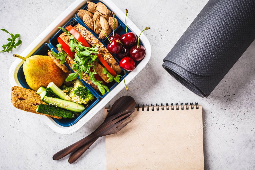 Sport food concept. Lunch box with heathy food, notebook and mat