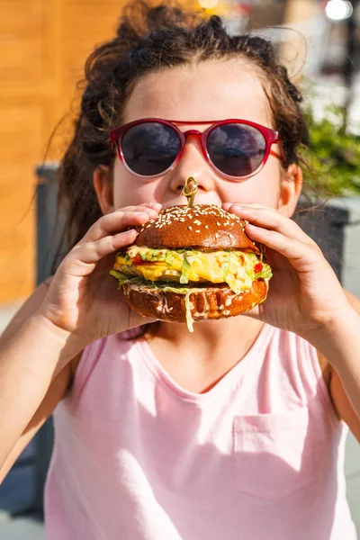 Little girl eating burger on the street.