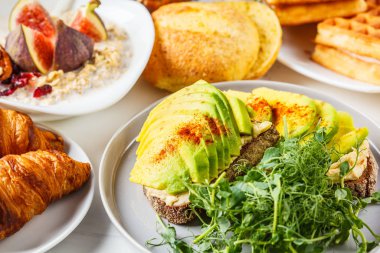 Avokado tost, yulaf ezmesi, waffle, kruvasan ile kahvaltı masası