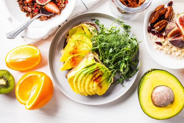 Avocado toast on breakfast table with oatmeal, granola, fruit — Stock Photo, Image