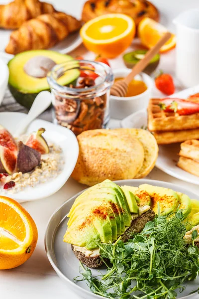 Ontbijttafel met avocado toast, havermout, wafels, croissants — Stockfoto