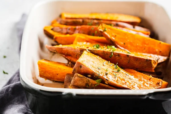Baked sweet potato slices with spices in oven dish.