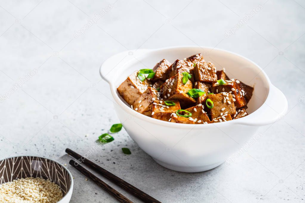 Teriyaki tofu with sesame seeds and green onion in white bowl. 