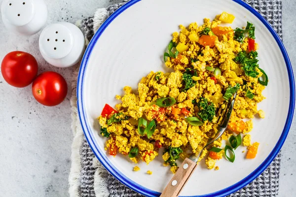 Tofu scramble with vegetables in a white plate, top view.