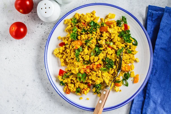 Tofu scramble with vegetables in a white plate, top view.