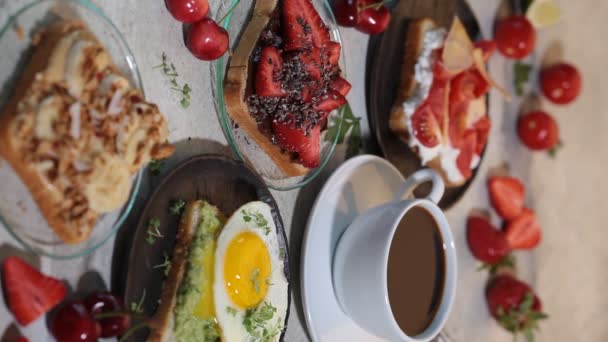 A agitar café, vertical. Café da manhã torradas diferentes com bagas, queijo, ovo e frutas, fundo cinza. Conceito de mesa de café . — Vídeo de Stock