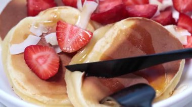 Çilekli ev yapımı krep ve beyaz kasede hindistan cevizi, çatal ve bıçakla kesilmiş..