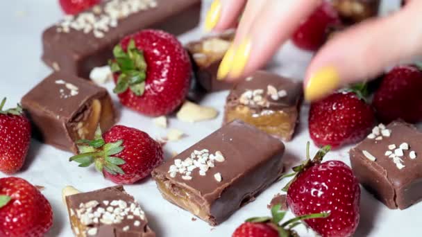 Jíst syrovou veganskou čokoládu a karamelové tyčinky s jahodovým, bílým pozadím. Zdravé dezerty koncept. — Stock video