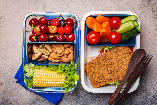 Lunch box with healthy fresh food. Sandwich, vegetables, fruits and nuts in food container, dark background.