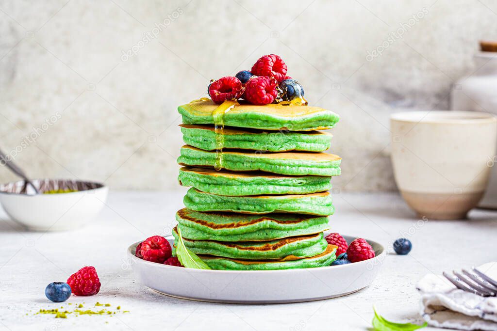 Matcha tea pancakes with berries, white background.