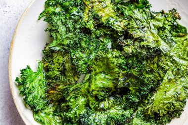 Beyaz tabakta tuzlu yeşil lahana cipsi. Sağlıklı vejetaryen gıda kavramı.