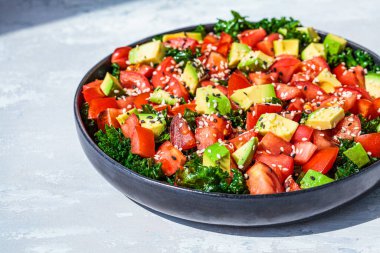 Domatesli lahana salatası ve siyah tabakta avokado. Sağlıklı çiğ vegan öğle yemeği konsepti.