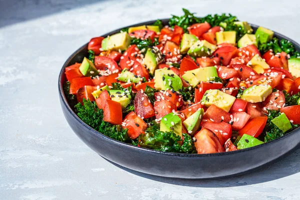 Kale salad with tomatoes and avocado in a black plate. Healthy raw vegan lunch concept.