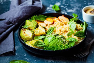 Vejetaryen yemek tabağı. Fırında kabaklı kinoa salatası, tatlı patates, avokado ve tahini sosu siyah tabakta..