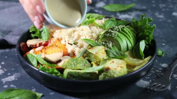 Salada de quinoa com abobrinha assada, batata-doce, abacate e molho de tahini em placa preta, fundo escuro. — Vídeo de Stock