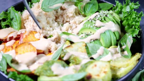 Salade de quinoa aux courgettes cuites au four, patate douce, avocat et vinaigrette tahini dans une assiette noire, fond sombre. — Video